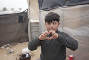 Image of a kid in a camp in Gaza forming a heart with his hand.