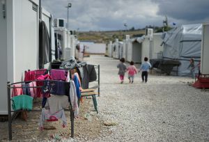 3 children back facing, walking about at an asylum seeker camp