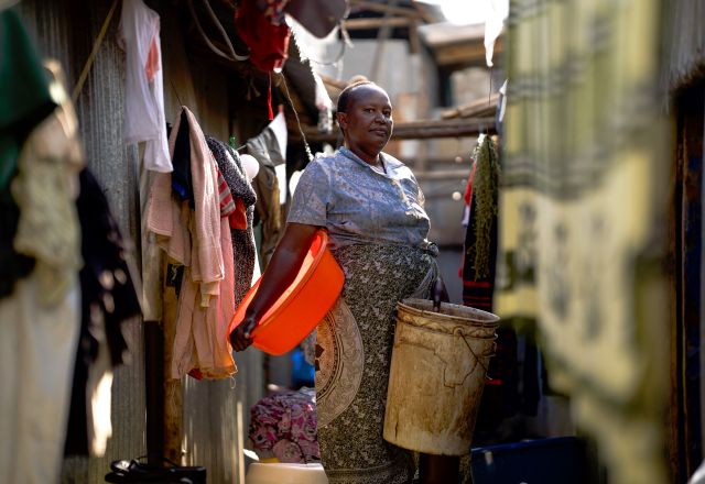 Woman standing between rows of hanging clothes with buckets in her hands in Narobi